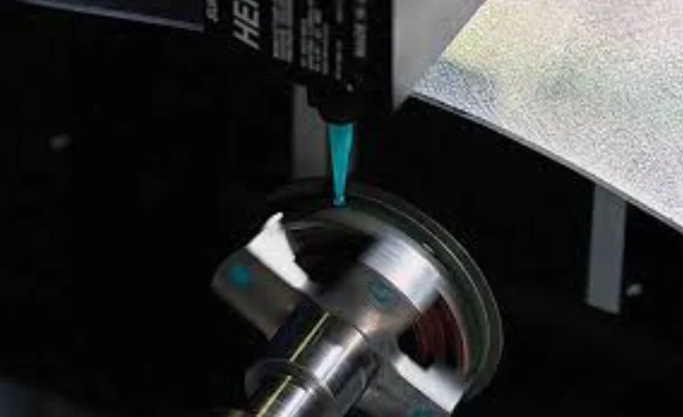 Automated adhesive dispensing nozzle applying material to a rotating metal part in industrial assembly