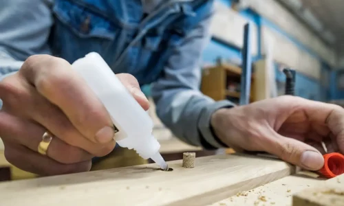 A technician applies precise adhesive from a Btektech squeeze bottle into a wooden dowel hole on a workbench, demonstrating reliable dispensing solutions for industrial bonding applications