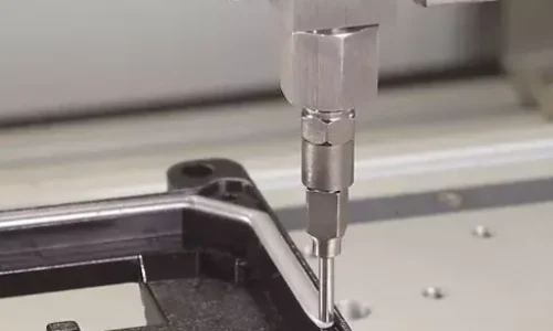 Precision robotic nozzle applying adhesive or sealant during automotive manufacturing, ensuring accurate bonding of plastic components in an automated assembly line