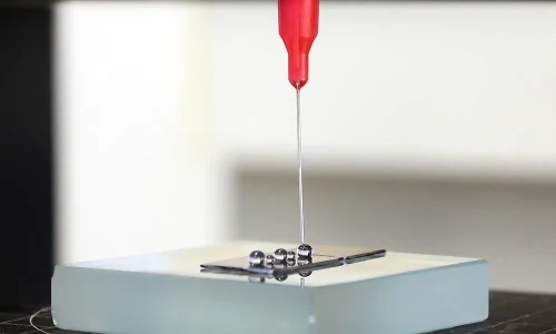 Red flexible dispensing tip creating uniform metallic micro-drops on a test surface